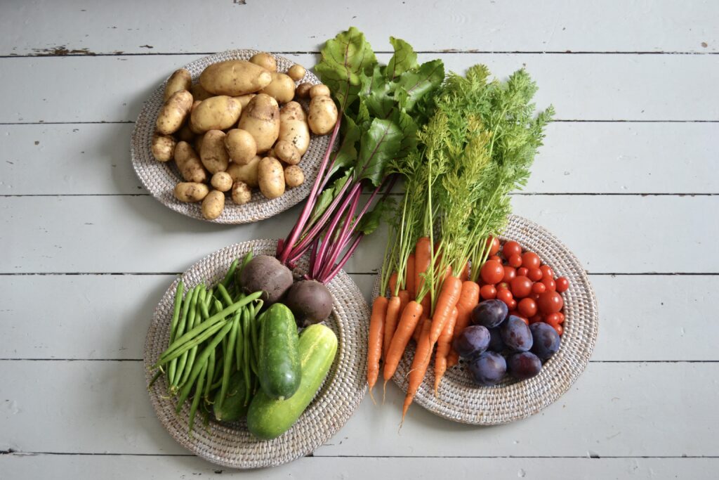 3 plates of colourful vegetables on a white wood background. The plates include beetroot, carrots, potatoes, and tomatoes. 