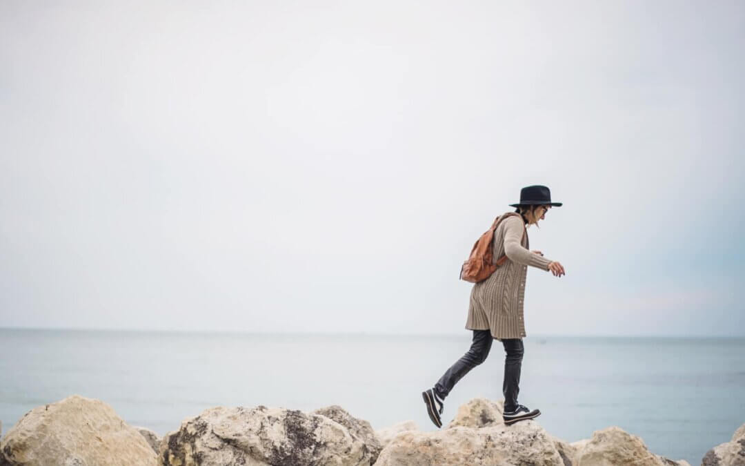 a woman walking across the rocks near the sea in summer