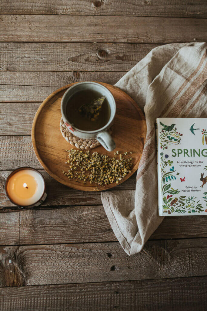 A spring inspired image with seasonal chamomile tea, a spring candles from The Smallest Light and a book of Spring poems and writing. 