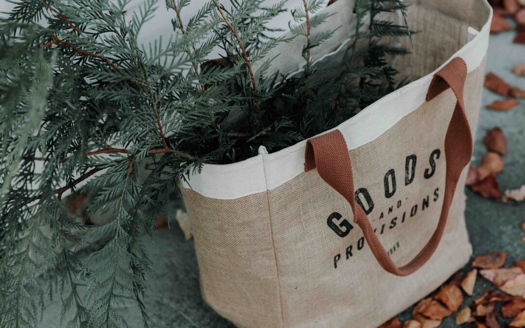 A picture of a woven shopping bag filled with pine branches. Image from Unsplash.